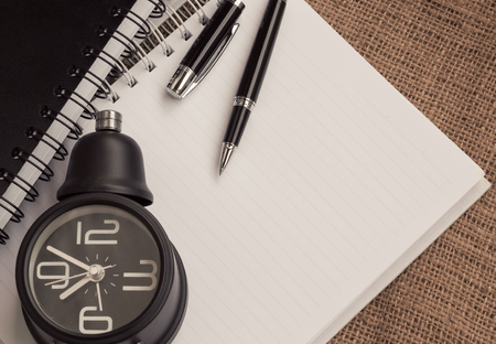 Alarm clock ,notebook and pen on sackcloth backgroundの写真素材