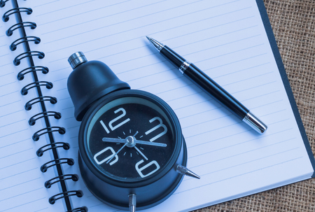 Alarm clock ,notebook and pen on sackcloth backgroundの写真素材