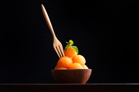 Organic cantaloupe melon in wooden bowl with wooden fork isolated on black background.の写真素材
