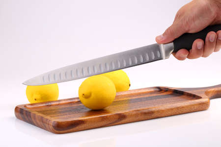 Organic fresh lemon on wooden tray with kitchen knife in hand isolated on white background.