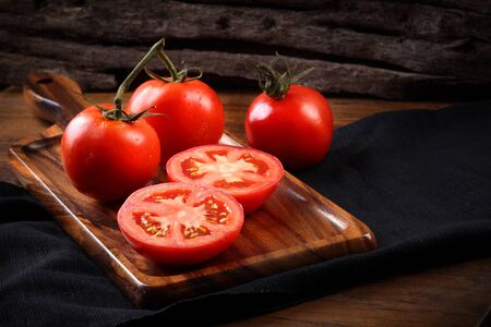 Cool fresh tomatoes, whole and half on wooden tray and wooden background.の写真素材
