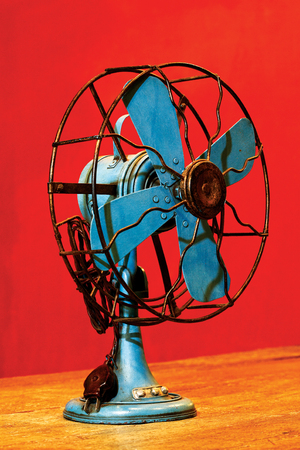 Blue antique rustic electric fans on wooden floor and red wall.の写真素材