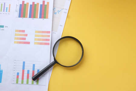 top view and flat lay magnifying glass and graph charts  document on yellow backgroundの写真素材
