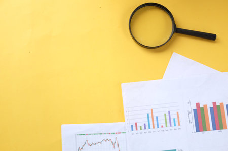 copy space magnifying glass and graph charts  document on yellow backgroundの写真素材
