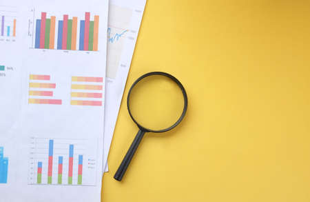 top view and flat lay magnifying glass and graph charts  document on yellow backgroundの写真素材