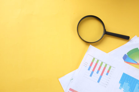 copy space magnifying glass and graph charts  document on yellow background