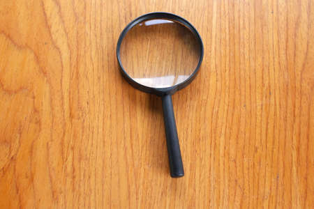 top view and flat lay black a magnifying glass on the brown wooden office desk backgroundの写真素材