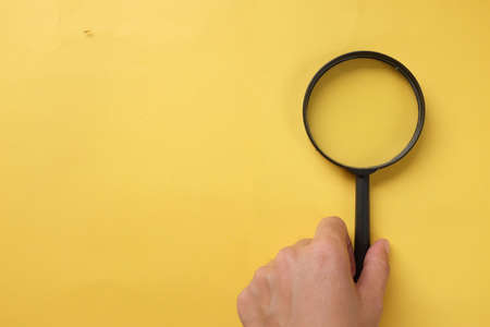 copy space  woman hand holding black a magnifying glass on the yellow office desk backgroundの写真素材