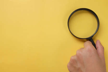 top view and flat lay man hand holding black a magnifying glass on the yellow office desk backgroundの写真素材