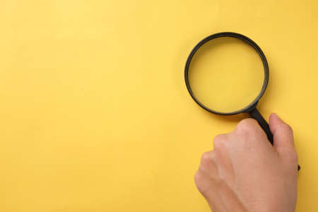 copy space  woman hand holding black a magnifying glass on the yellow office desk backgroundの写真素材
