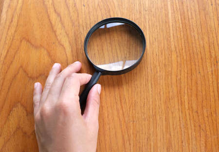 copy space woman hand holding black a magnifying glass on the brown wooden office desk backgroundの写真素材