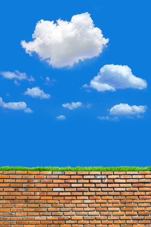 old red brick wall with grass over cloudy and blue sky background in day lightの写真素材