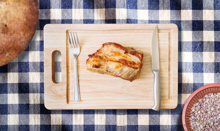 roast pork neck on cutting board with knife and fork on blue gingham cloth backgroundの写真素材