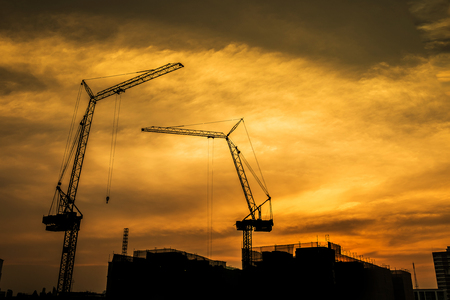 Industrial construction cranes and building silhouettes over sunsetの写真素材