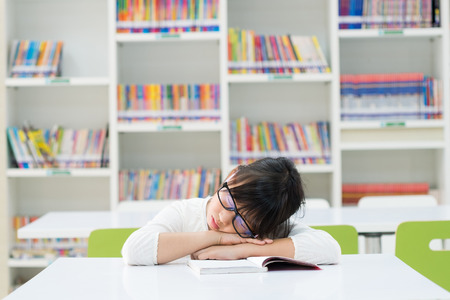 tired teenage girl napping on a book in libraryの写真素材