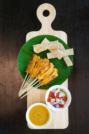 overhead view pork satay with delicious peanut sauce, onion and cucumber on wooden cutting board in dark backgroundの写真素材