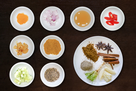 various herbs cinnamon, star anise, sarlic, black pepers, corriander root  in white plate on black brown wooden backgroundの写真素材