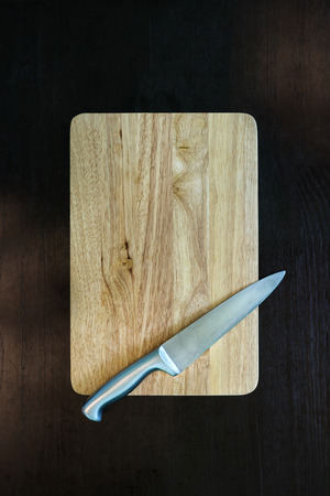 stainless  kitchen knife on wood cutting board on dark background with sunlight through from windowの写真素材