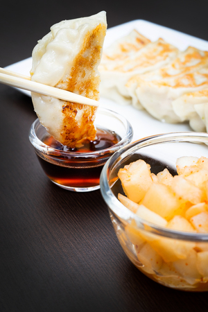 wood chopstick holding a dumplings snack in sauce on dark background tableの写真素材
