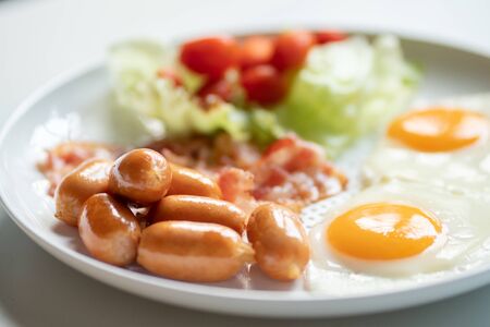 selective focus on sausage and fried eggs and bacon in white plate  on table for breakfast serveの写真素材