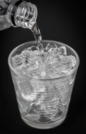 puring water Into glass with ice on dark backgroundの写真素材