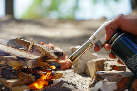 Hand holds manul gas burner near firewood