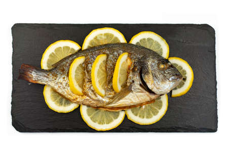 Baked grilled cooked dorado fish and lemon lie on a black stone slate boardの写真素材