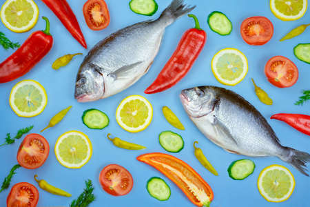 Dorado fish and vegetables: cucumber, tomato, pepper, lemon lie on a blue background. Background...