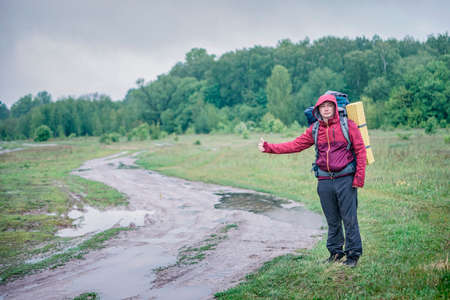 Guy tourist hiker walks along the road with a backpack in a red