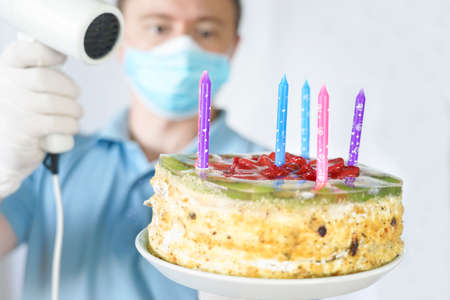 A guy in a mask and gloves blows out the candles on a birthday cake during covid-19 quarantine.