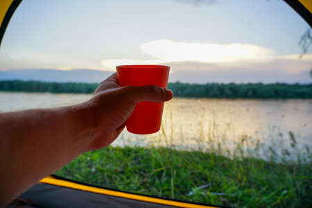 The hand from the tent holds a glass on the background of the riverの写真素材