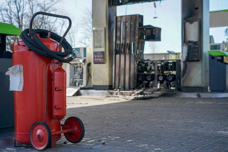 Red fire extinguisher in the parking lot after the fire. Gas station with a broken station from a shell explosion. Exploded gas station during the war.の写真素材
