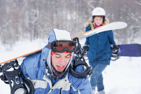 A guy and a girl in snowboarding clothes are walking along the ski slope. They are holding a...