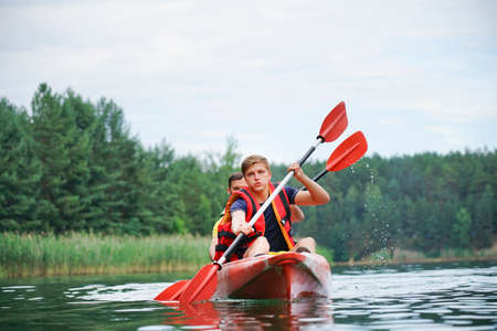 two guys in a red kayak on the river, in life jacketsの写真素材