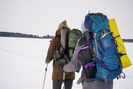 Two guys walk through loose snow during a winter expedition. They carry large backpacks, warm...