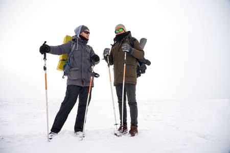 Two guys walk through loose snow during a winter expedition. They carry large backpacks, warm...