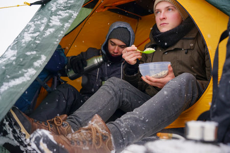 The guys are sitting in a tent, preparing food during a winter hike. Near the tent in the snow lies...