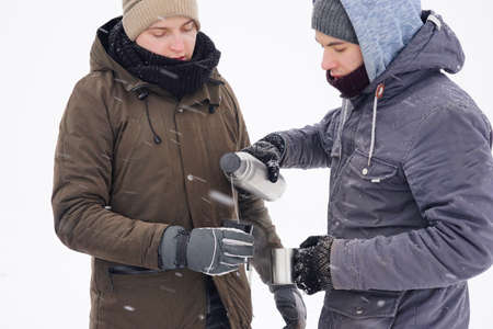 he guys drink hot tea from thermo mugs and pour water . They stand by the tent during the winter...
