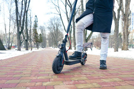 Scooter in the park near the snow. Riding a scooter during the cold season. A guy stands near a scooter next to a snowdriftの写真素材