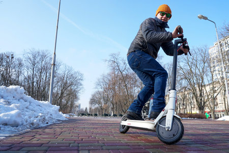 The guy rides and jump an electric scooter in the spring in the park.