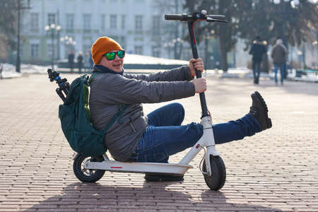 Guy photographer sits on an electric scooter in the spring in the park. He is wearing a warm jacket...