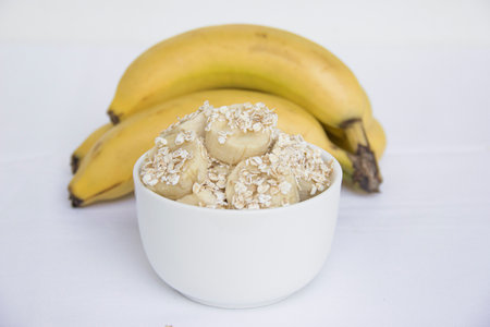 A bunch of bananas and a sliced banana with oats in a jar on the table.の写真素材