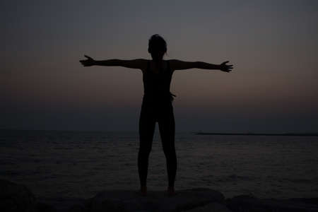 young woman doing yoga on coast of sea on beach