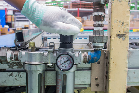 The hand of technician adjust the pressure setting of the wind on regulator. In the pneumatic system
