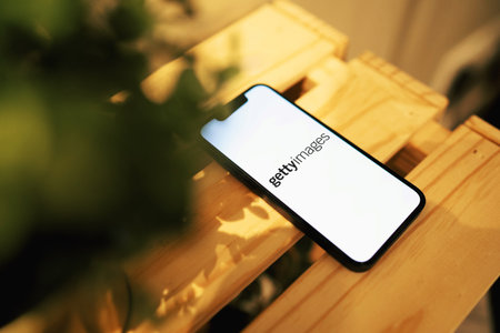 October 3, 2022: Gettyimages logo on smartphone screen. Smartphone on wooden table with plant.のeditorial素材