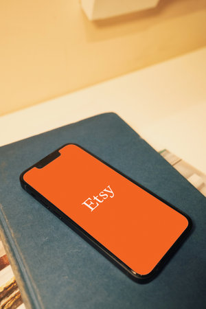 October 6, 2022: Etsy logo on smartphone screen. Smartphone on book.のeditorial素材