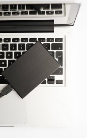 Metallic external hard drive, with cable (usb) on top of laptop, on the white office table. Top viewの写真素材