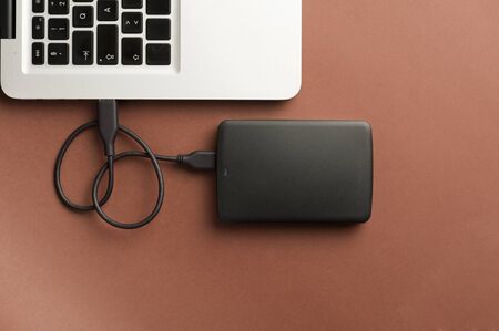 black external hard drive, partial laptop view, brown background, office concept.top view