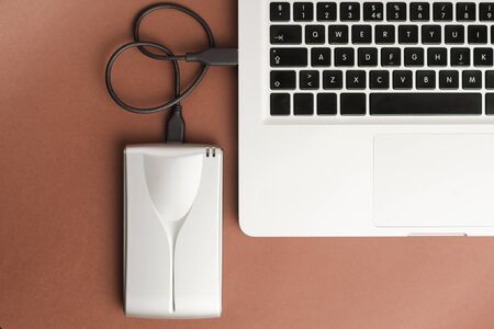 Aluminum external hard drive with cable (usb) connected to laptop, on brown office table.Top viewの写真素材