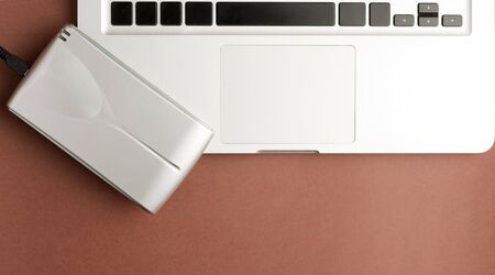 Aluminum external hard drive, on top of laptop, brown background, office concept.top viewの写真素材